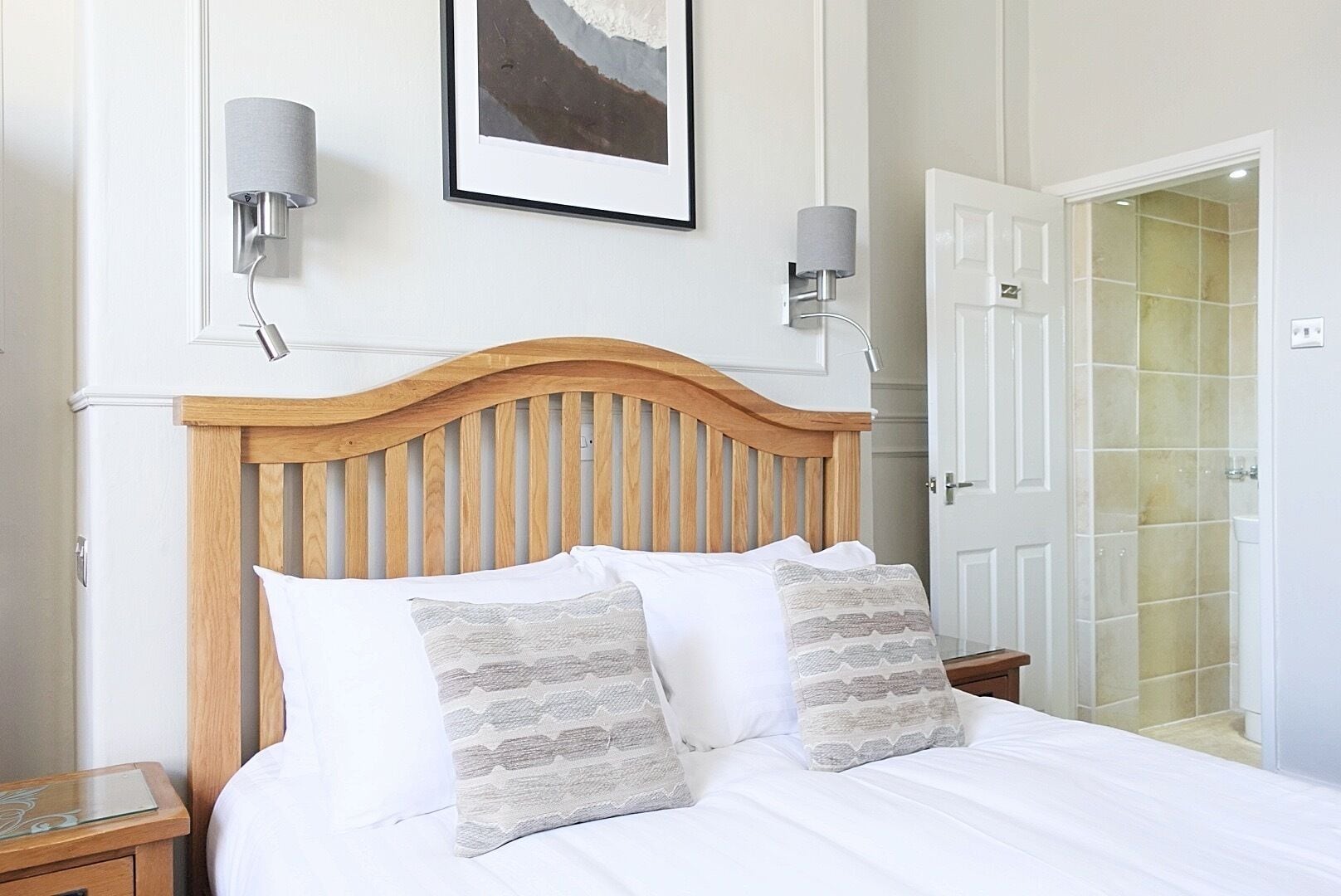 A neatly made bed with a wooden headboard, two bedside lamps, and a framed picture on the wall.