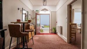 A hotel lobby with a red carpet, bar area with stools, a mirror, and a view of the sea through an open door. - The Kendrick Exclusively for Adults (Llandudno)