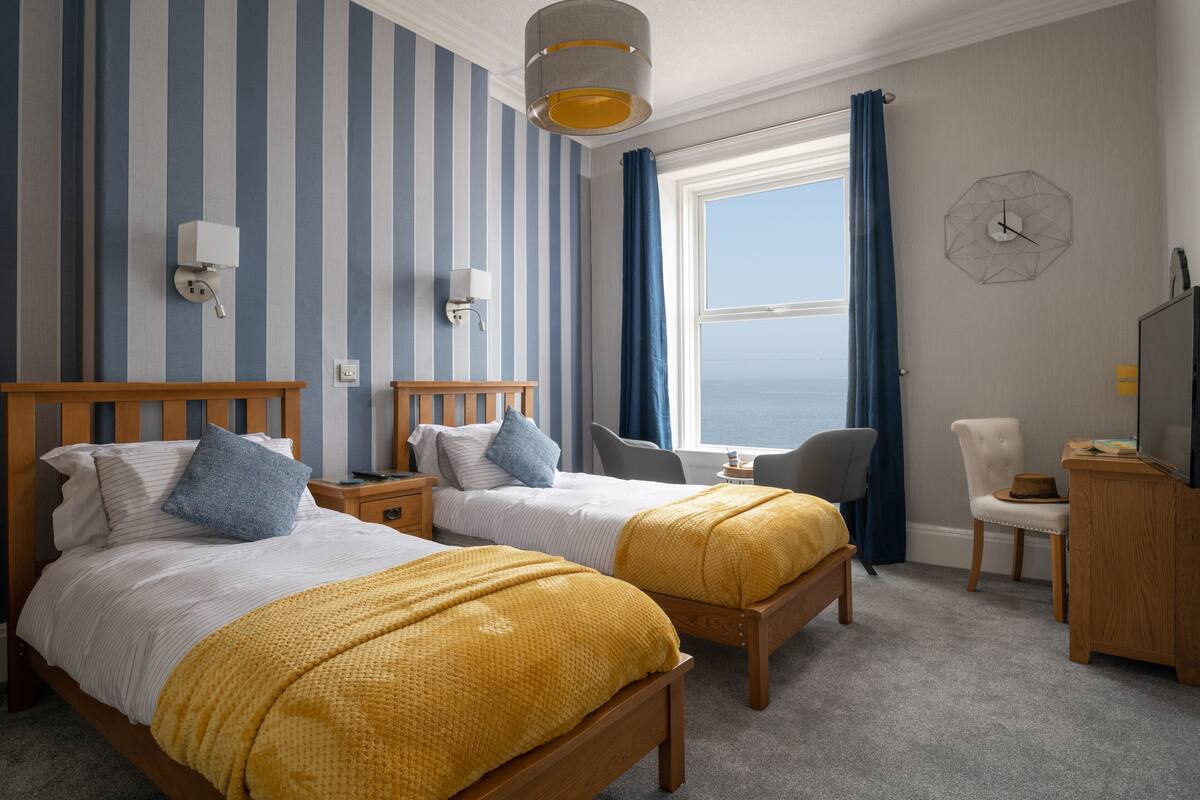 Et hotelværelse med to senge, et skrivebord, en stol, et fjernsyn og havudsigt.