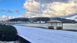 A snow-covered promenade with a small shelter and a distant town. - The Kendrick Exclusively for Adults (Llandudno)