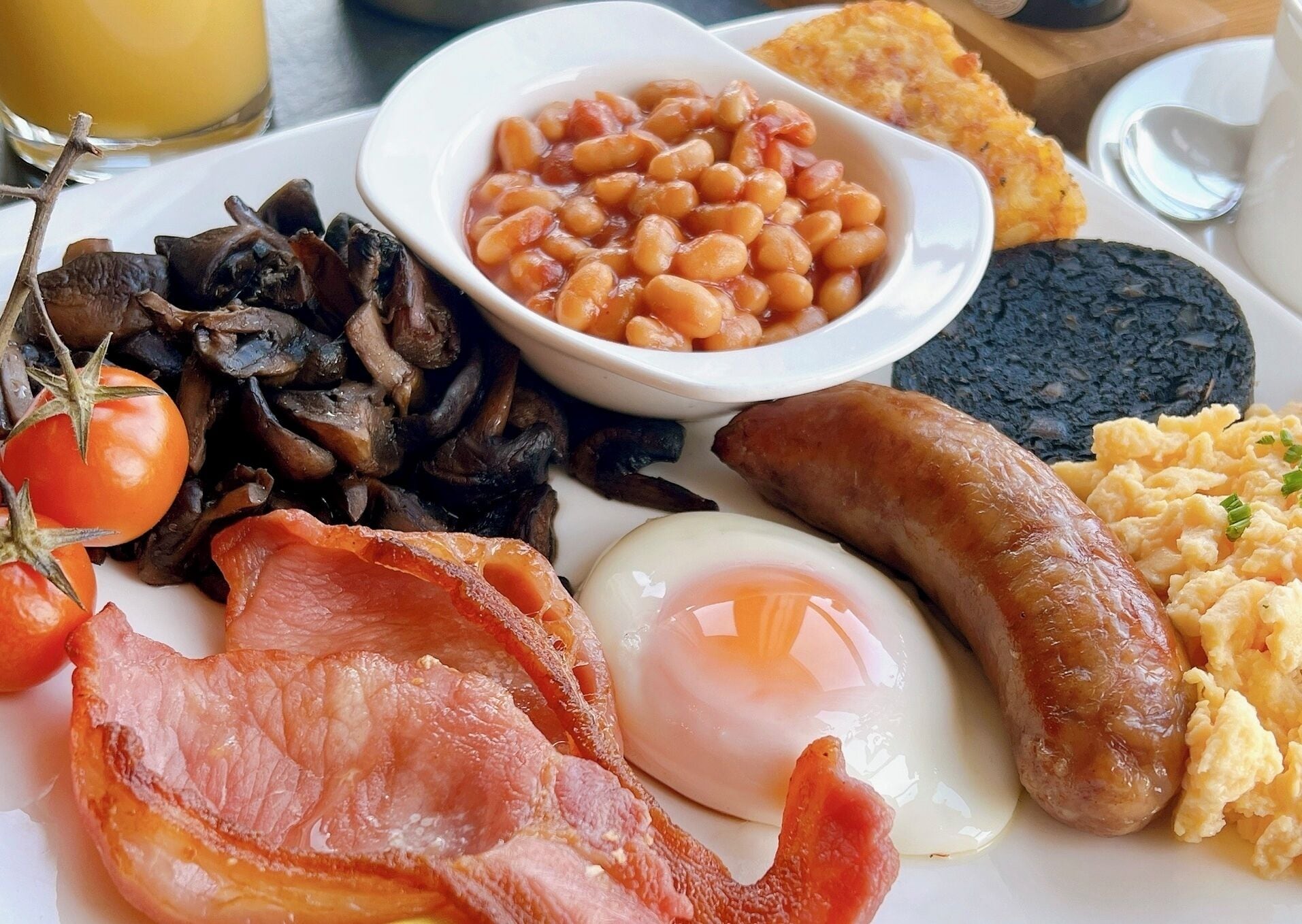 A breakfast plate with eggs, bacon, sausages, mushrooms, beans, toast, and scrambled eggs.