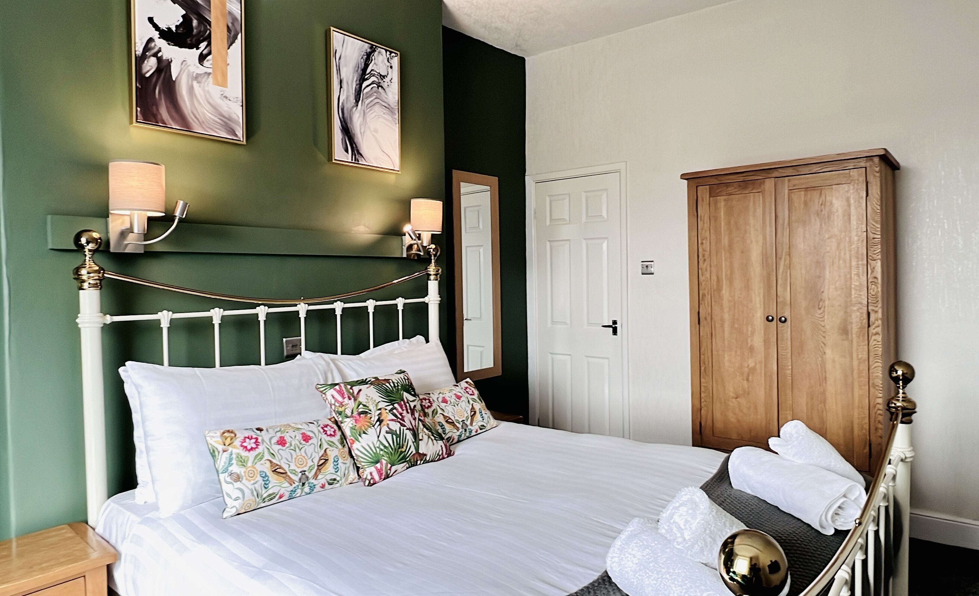 Una cama bien hecha con ropa de cama blanca y almohadas con motivos florales, un armario de madera y dos lámparas de pared.