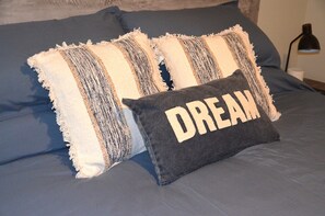 A bed with blue bedding and two pillows, one with a frayed edge and the other with the word "DREAM" on it. - Trendy Escape (Enterprise)