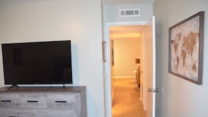 Habitación de hotel con televisor sobre un aparador de madera, una puerta que da a un pasillo y un mapa mundial en la pared.
