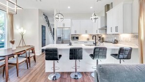 A modern kitchen with white cabinets, a central island, and bar stools. - Spacious 5BR Mid-City home with balcony & backyard oasis. Sleeps 10, 4 kings, steps to streetcar & parades (New Orleans)