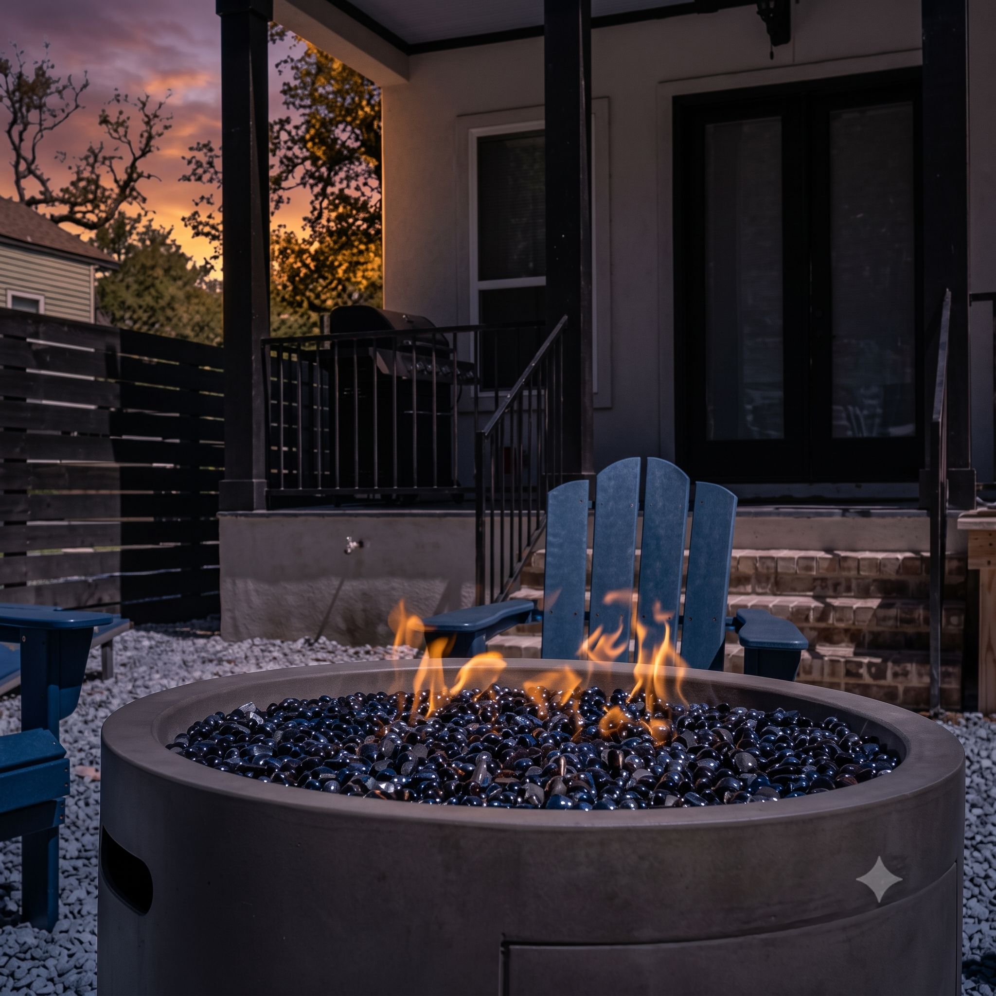 A fire pit with a star design, surrounded by a gravel area with blue chairs.