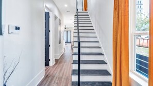 A modern staircase with a black railing, leading to a second-floor landing. - Spacious 5BR Mid-City home with balcony & backyard oasis. Sleeps 10, 4 kings, steps to streetcar & parades (New Orleans)