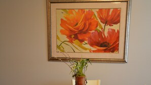 Ein Esstisch mit Blumen in einer Vase, darüber ein gerahmtes Kunstwerk und weiße Stühle.