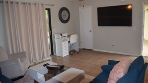 Ein Wohnzimmer mit Deckenventilator, Flachbildfernseher, weißem Schreibtisch und blauem Sofa.