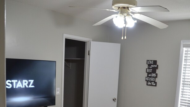 Ein Schlafzimmer mit einem Bett, einem Fernseher auf einer Kommode, einem Deckenventilator und einem Kleiderschrank.