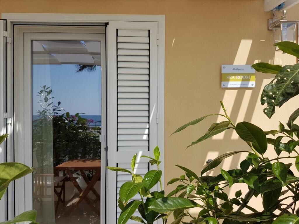 Habitación de hotel con puerta corrediza de vidrio que da a un balcón, un letrero que indica habitación con vista al mar y una planta en maceta al frente.