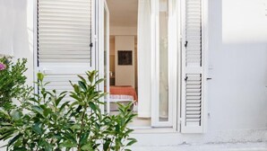 A white building with a sliding glass door leading to a bedroom with a bed and a framed picture on the wall. - Break For Two (Agropoli)