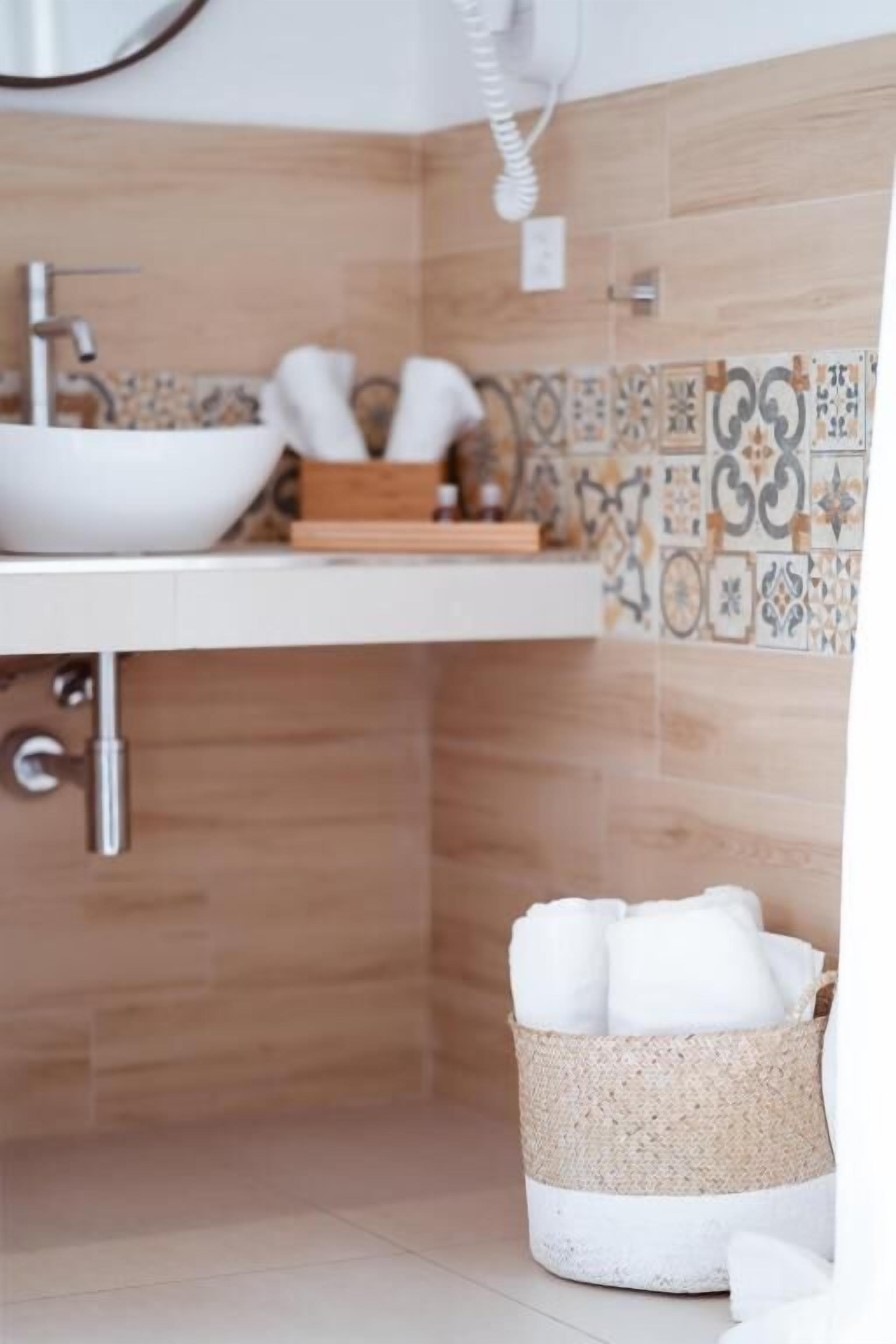 Un baño con lavamanos blanco, baldosas de madera y una cesta de mimbre con toallas.