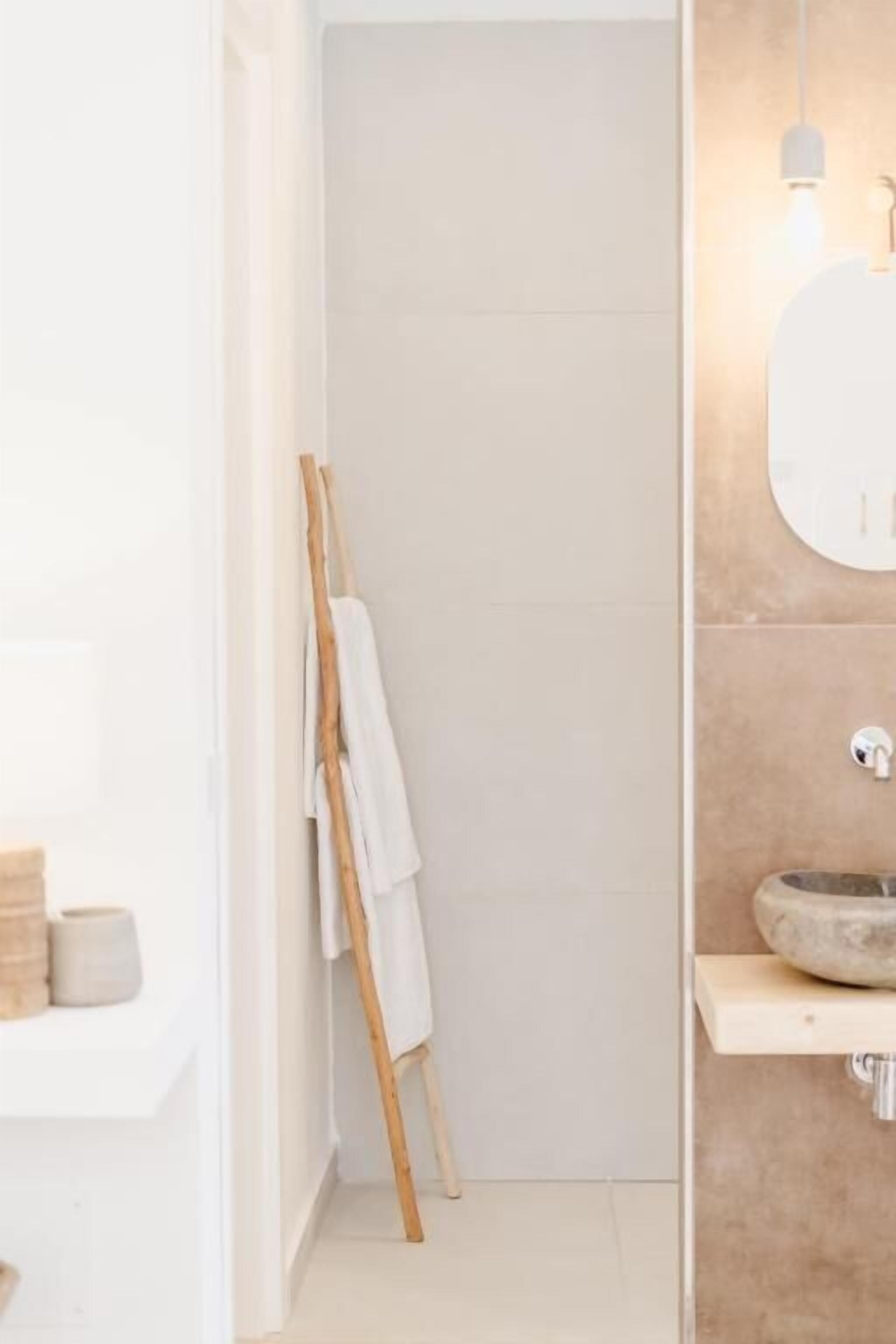 A modern bathroom with a large mirror, a round sink, and a wooden easel with a white towel.