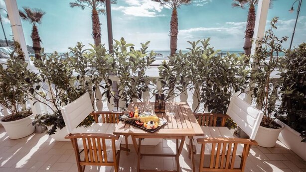 A wooden table and chairs set up on a terrace with potted plants and a view of the sea. - Break For Two (Agropoli)