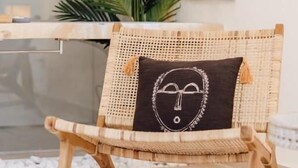 A wicker chair with a dark cushion featuring a white design, positioned in a room with a large green plant and a window in the background. - Break For Two (Agropoli)