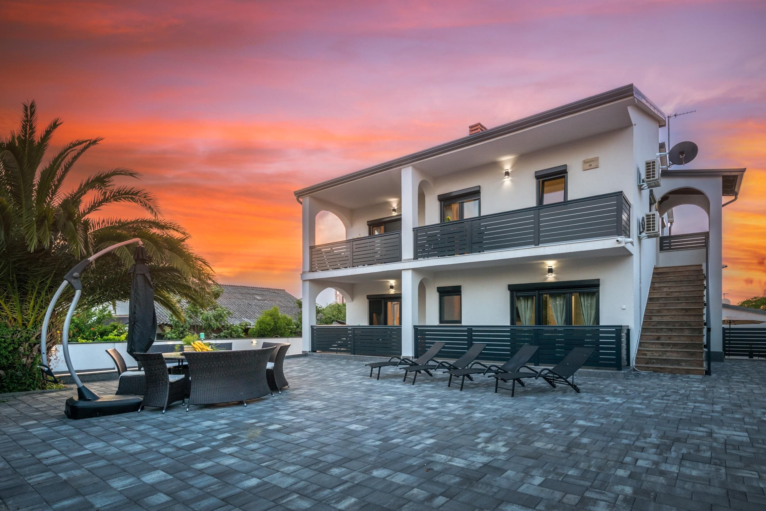 A two-story building with a balcony, outdoor seating, and a sunset view.
