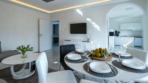 A modern dining area with a round table set for four, a kitchen visible through an archway, and a flat-screen TV mounted on the wall. - Villa LiLi Apt 2 with balcony (Poreč)