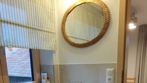 A bathroom with a white sink, mirror, and cabinet, a window with striped curtains, and a tiled floor. - Appartement am Weißbach - Urlaub im Pfrontener Tal (Pfronten)