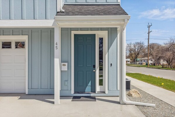 Una casa de dos pisos con fachada azul claro, una puerta principal azul oscuro y un garaje con puerta blanca.
