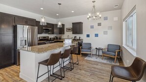 A modern kitchen with a central island, bar stools, and a seating area with two chairs. - My Glacier Getaway - 3 min to downtown Kalispell! (Kalispell)