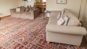 A living room with two sofas, a patterned carpet, a dining area with chairs, and a table. - Causeway Cottage (Berwick-upon-Tweed)