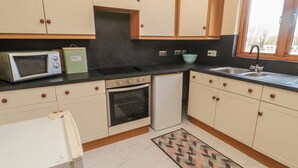 A kitchen with white cabinets, a microwave, an oven, a refrigerator, a sink, and a window. - Causeway Cottage (Berwick-upon-Tweed)