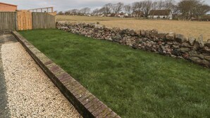 A grassy yard with a stone wall, wooden fence, and a gravel path. - Causeway Cottage (Berwick-upon-Tweed)
