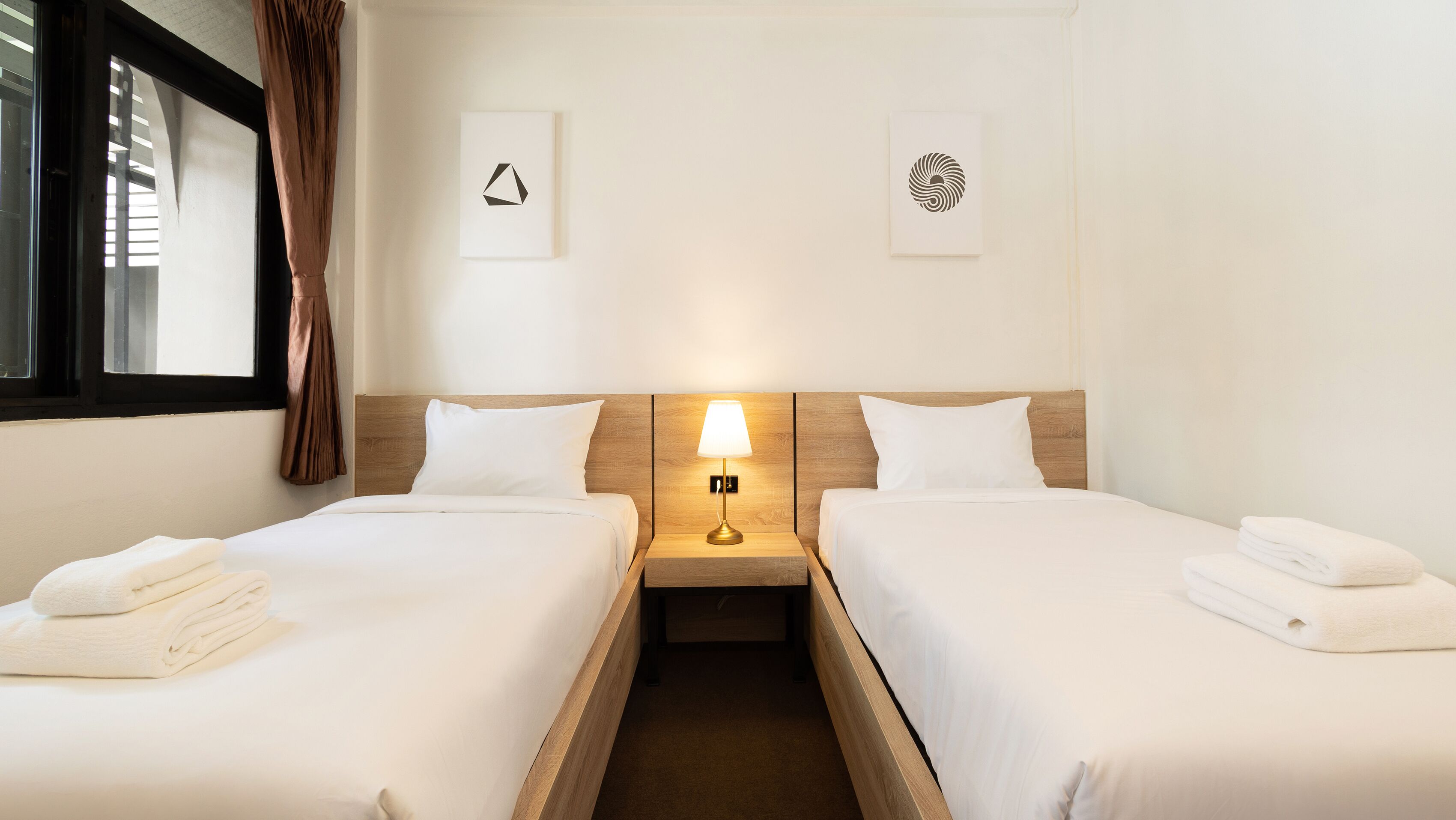A hotel room with two beds, a nightstand with a lamp, and artwork on the walls.