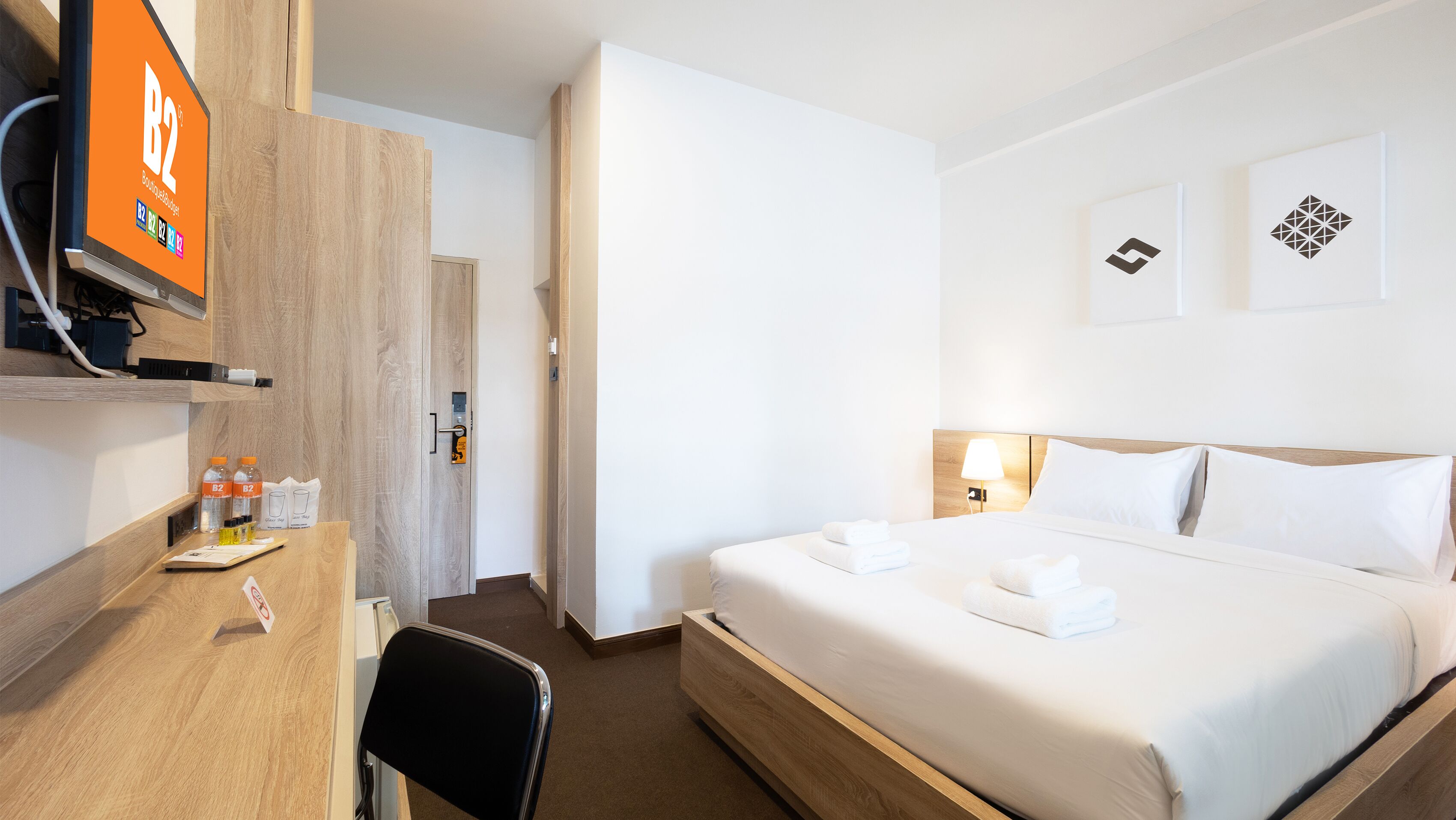 Una habitación de hotel con una cama, un escritorio con monitor de computadora, una silla y una puerta.