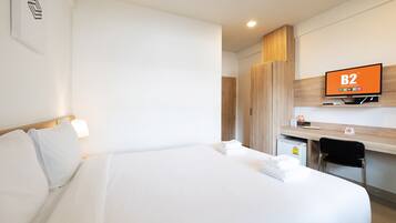 Una habitación de hotel con cama, escritorio, silla, televisor y armario.