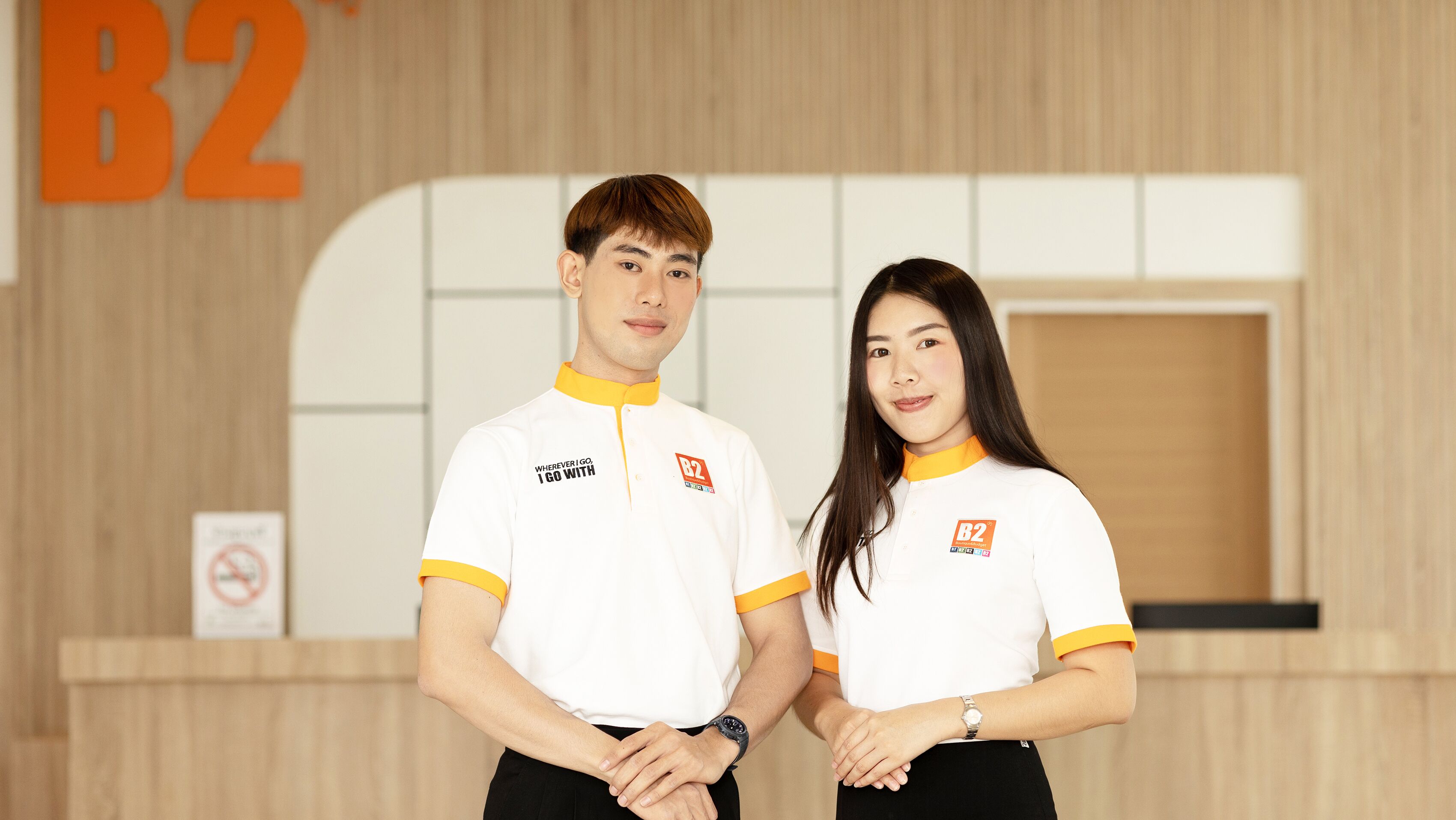 Two people standing in front of a reception desk with a sign that reads "B2".