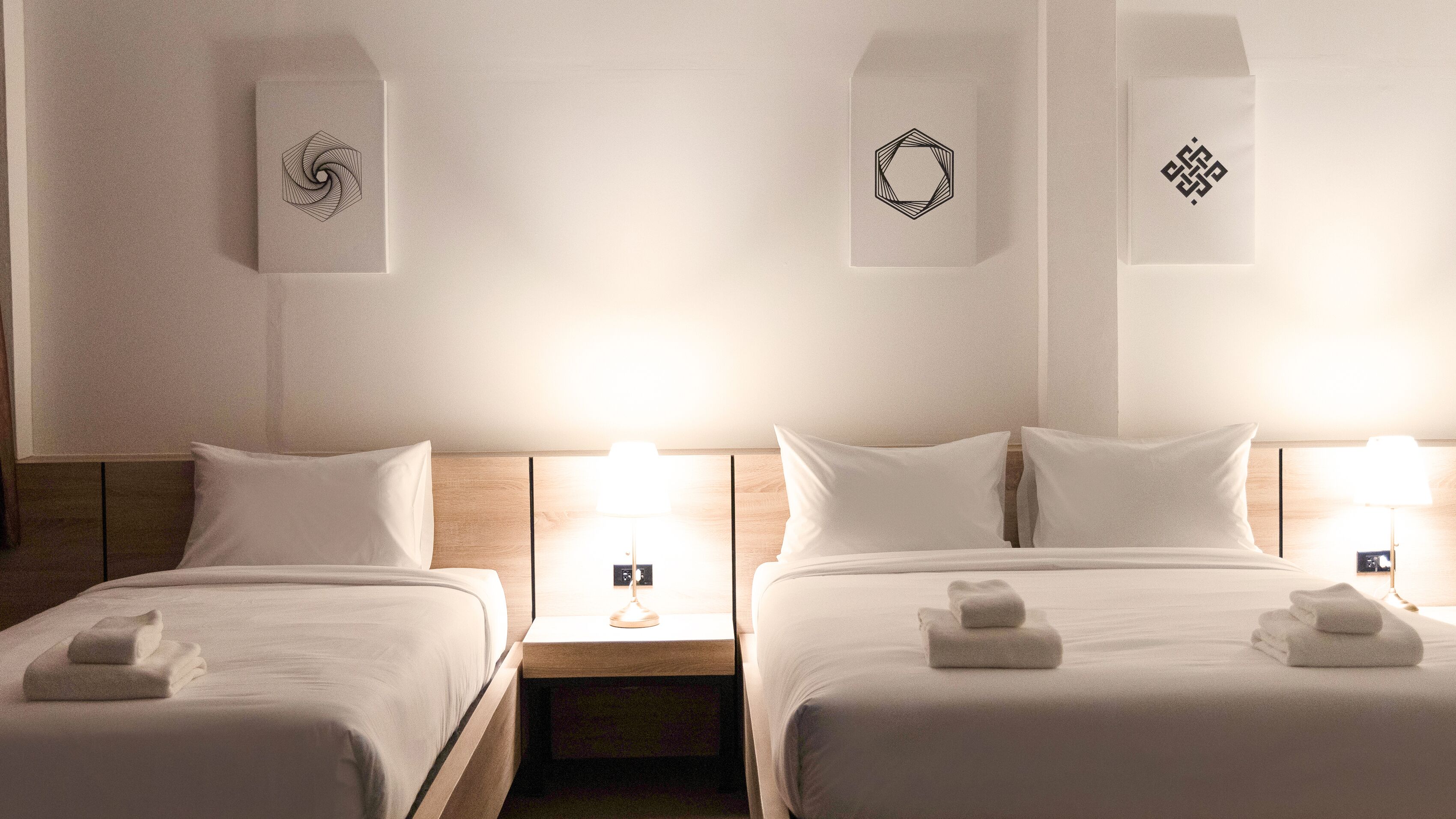 A hotel room with two beds, each with a headboard, bedside tables, and lamps. There are towels folded on the beds.