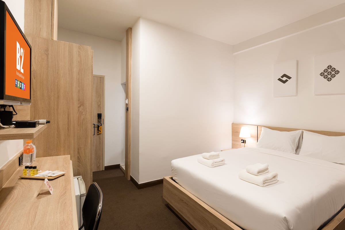 Habitació d'hotel amb un llit, un televisor, una taula de nit amb articles de tocador, i una porta que dona a una altra habitació.