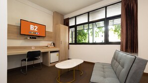 Habitación de hotel con escritorio, silla, sofá y televisor mostrando 'B2 Boutique & Budget'.