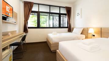 A hotel room with two beds, a desk, a chair, a TV, and a window with curtains.