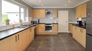 A modern kitchen with wooden cabinets, a stainless steel range hood, and a large window. - Coedfan (Ruthin)