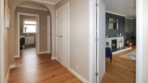 A hallway with wooden flooring, white doors, and a ceiling light fixture. - Coedfan (Ruthin)