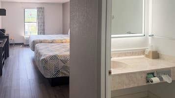 Une chambre d’hôtel avec deux lits, un bureau, une fenêtre avec des rideaux et une salle de bain équipée d’un miroir et d’un distributeur de serviettes.