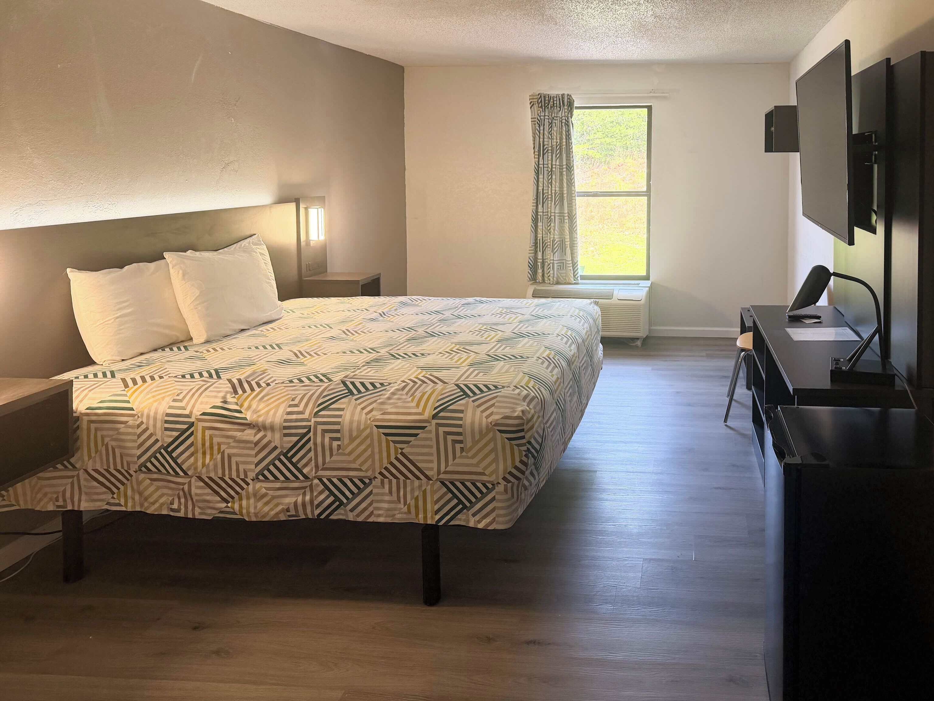 Ein Hotelzimmer mit Bett, Schreibtisch, Stuhl, Fernseher und einem Fenster mit Vorhängen.