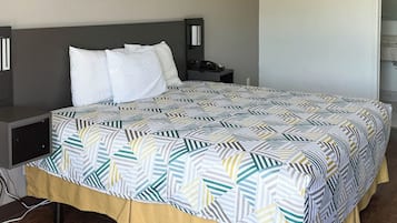A neatly made bed with a patterned bedspread and pillows, a bedside table with a lamp, and a wall-mounted phone.