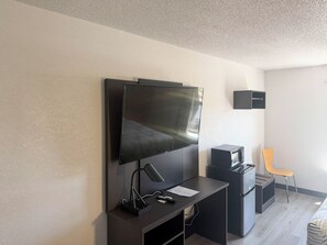 A modern room with a flat-screen TV mounted on the wall, a desk with a lamp, a microwave, and a chair. - Motel 6 Fancy Gap, VA (Fancy Gap)
