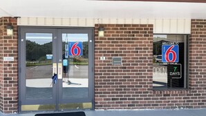 A motel entrance with a brick facade, double doors, and a welcome sign. - Motel 6 Fancy Gap, VA (Fancy Gap)