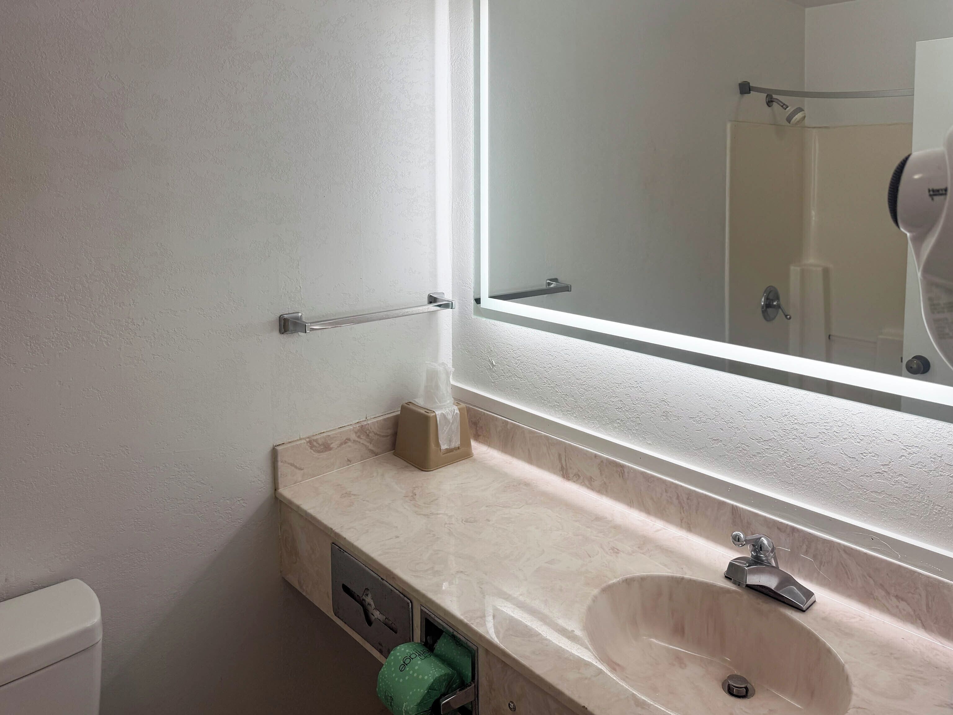 Un baño con lavamanos de mármol, un espejo, dispensador de toallas y un inodoro.