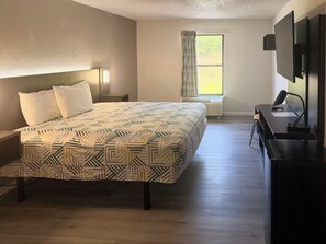 A bedroom with a bed, a desk, a chair, a window with curtains, and a wall-mounted TV. - Motel 6 Fancy Gap, VA (Fancy Gap)