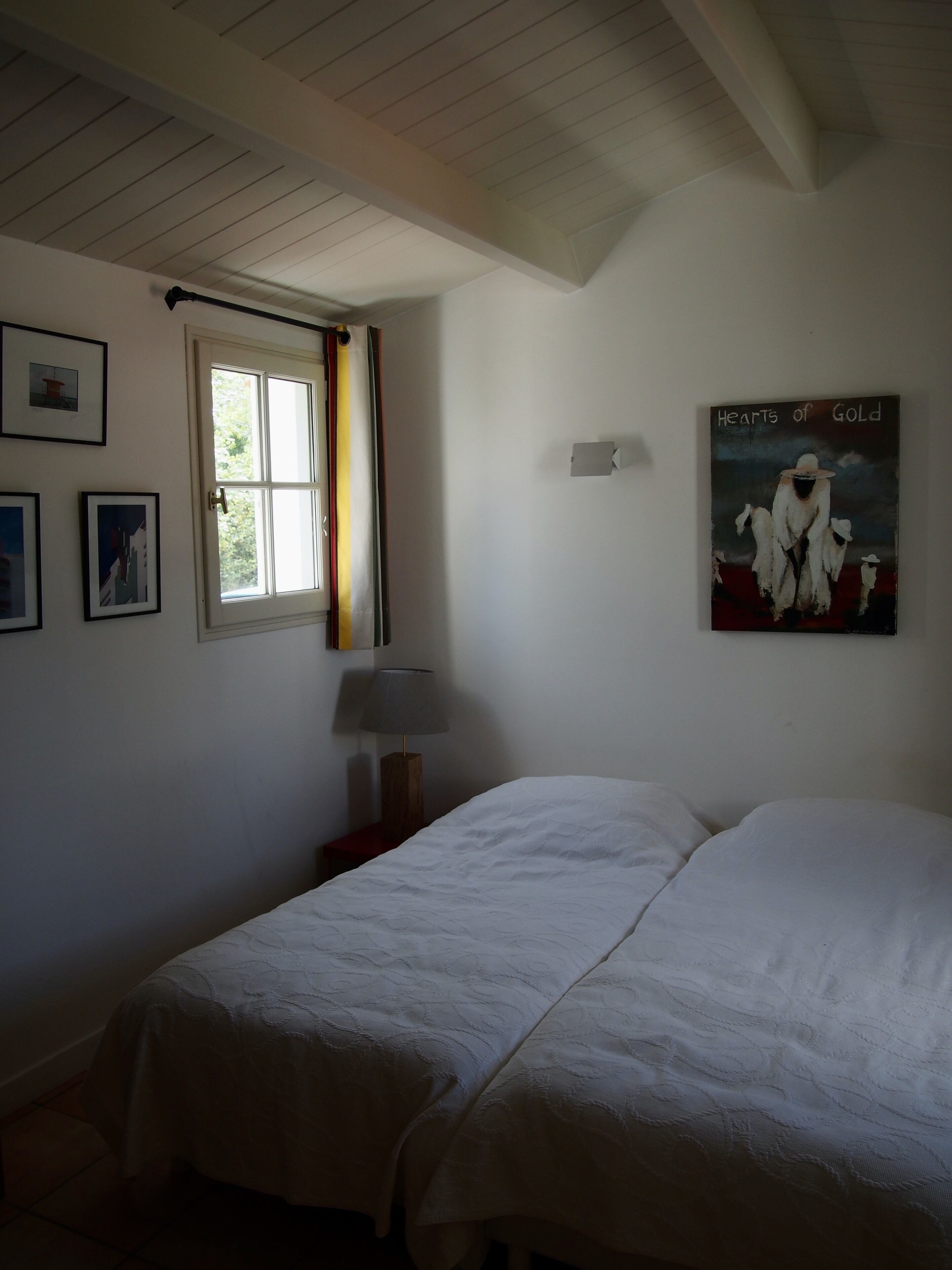 Un dormitorio con dos camas, una ventana con cortina, una lámpara y un cuadro en la pared.