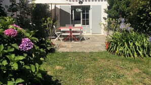 A patio area with a table and chairs, surrounded by lush greenery and flowers. - Charming house close to the beach, (L'Île-d'Yeu)