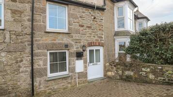 A stone house with a brick pathway, a white door, and a small window with shutters.