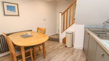 A dining area with a wooden table and chairs, a kitchen with a sink and cabinets, and a staircase leading to another level.