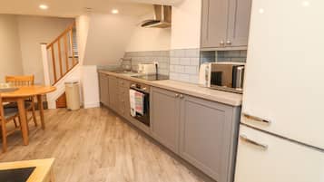 A compact kitchen with grey cabinets, a stainless steel range hood, a microwave, and a built-in oven.